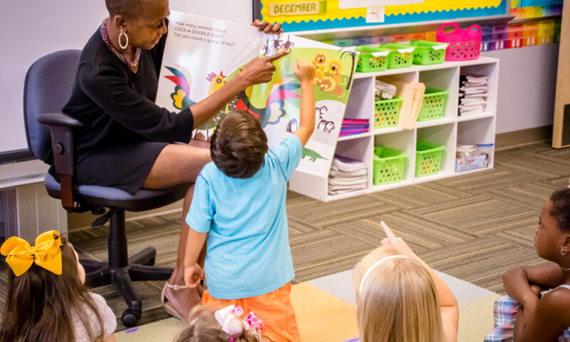 A teacher reads an ORIGO Big Book to a class. The teacher and a student point to an illustration on the page.