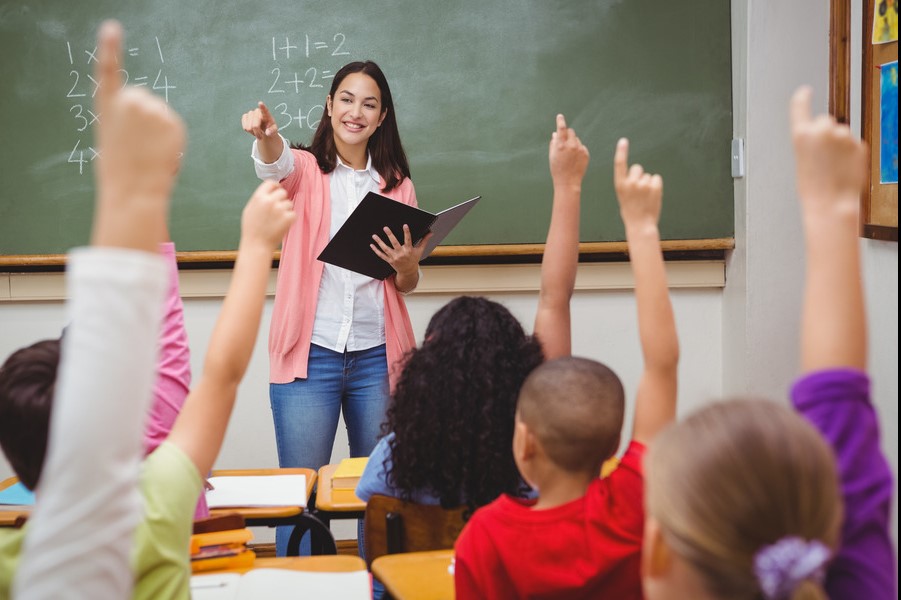 teacher in classroom with students raising hands